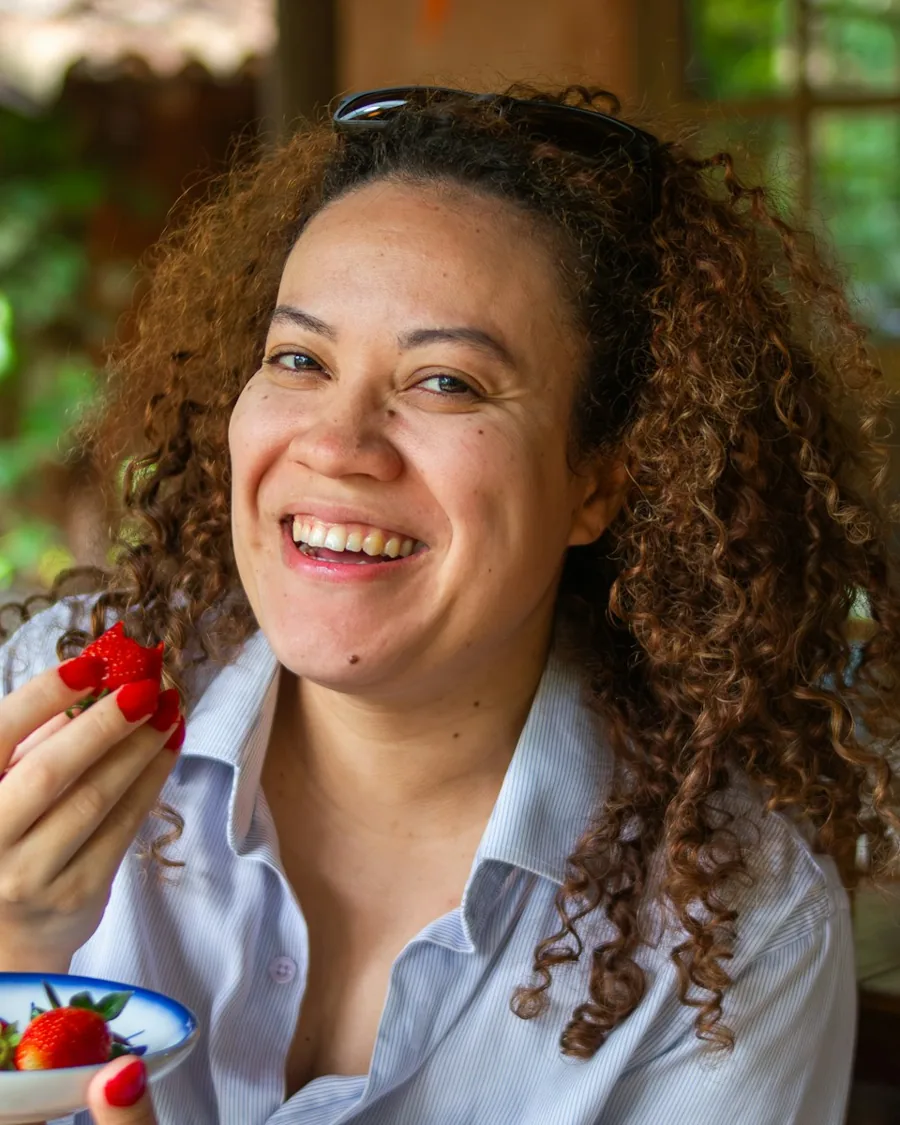 A smiling woman with curly hair eating strawberries
